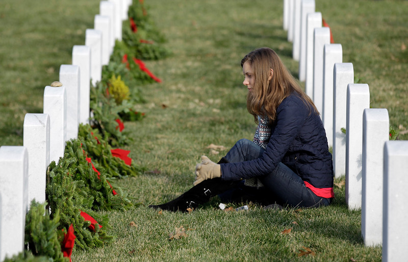 Lianna Bennett sits at the headstone of her grandfather U.S. Army Col. William W. Etchemendy during Wreaths Across America's 150th anniversary, Saturday, Dec. 13, 2014, at Arlington National Cemetery in Arlington, Va. (AP Photo/Luis M. Alvarez)